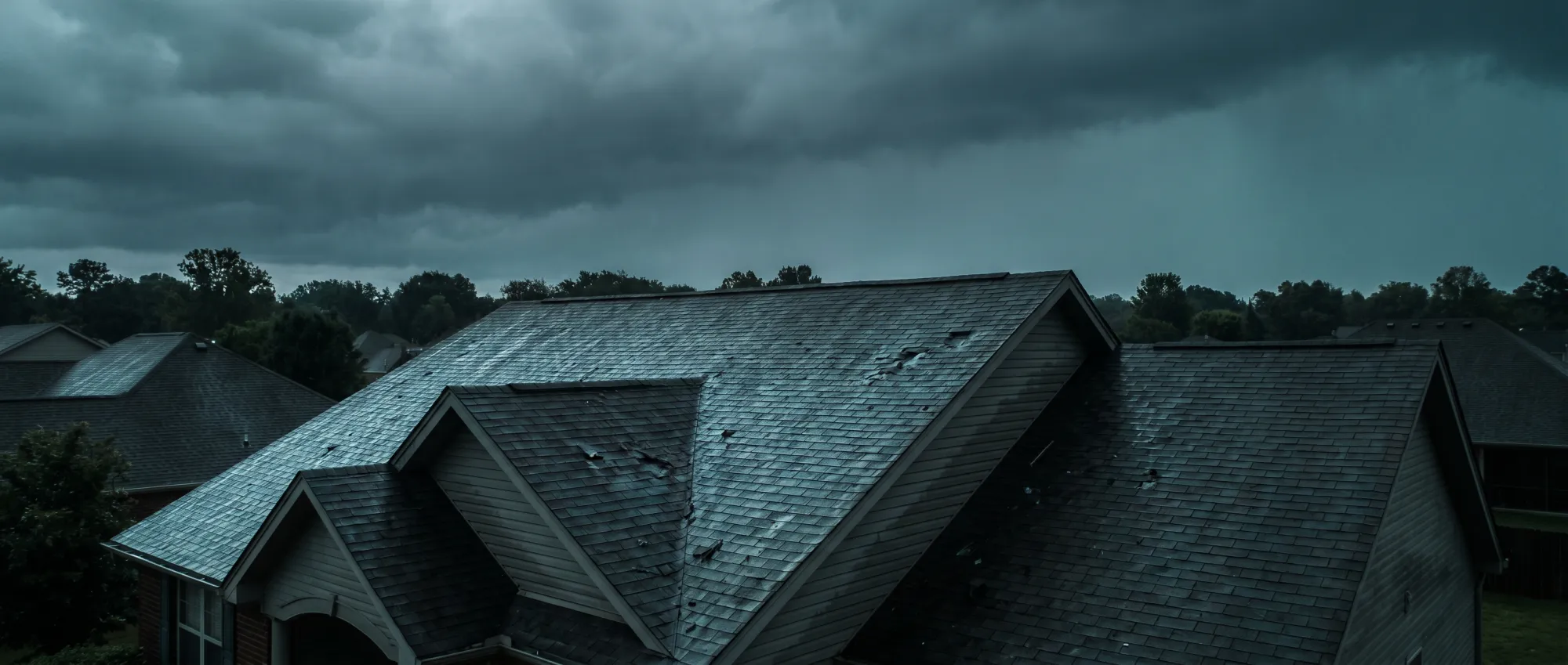 Hail-damaged suburban roof under a heavy storm sky